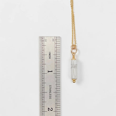 Gold necklace with a clear pendant next to a ruler on a white background