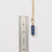 Necklace with a blue pendant next to a ruler on a white background