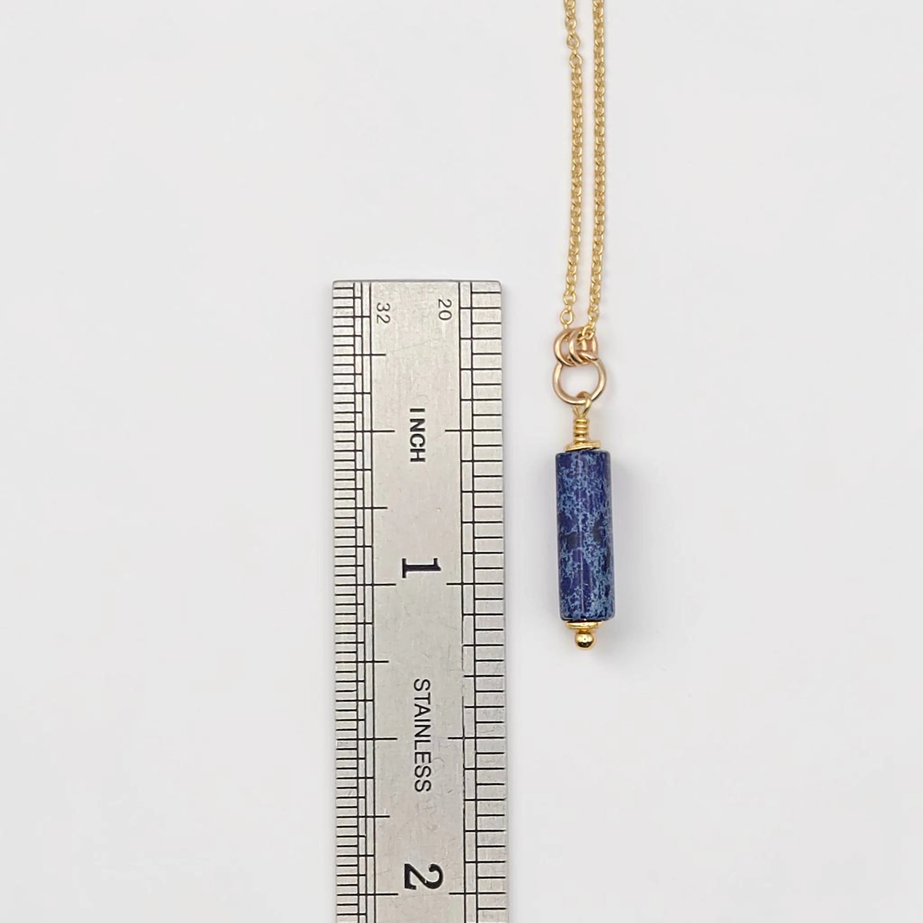 Necklace with a blue pendant next to a ruler on a white background