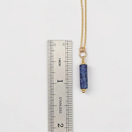 Necklace with a blue pendant next to a ruler on a white background