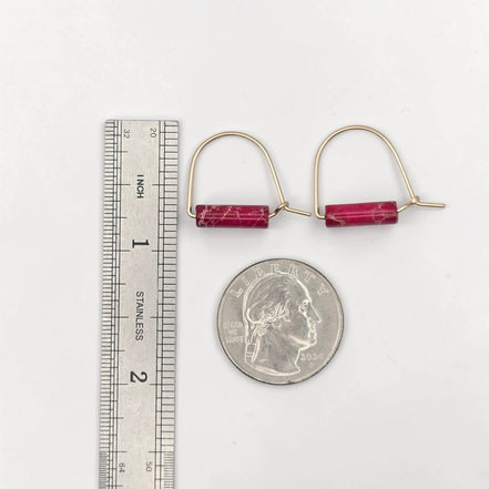 Gold earrings with red stones next to a ruler and quarter for scale on a white background