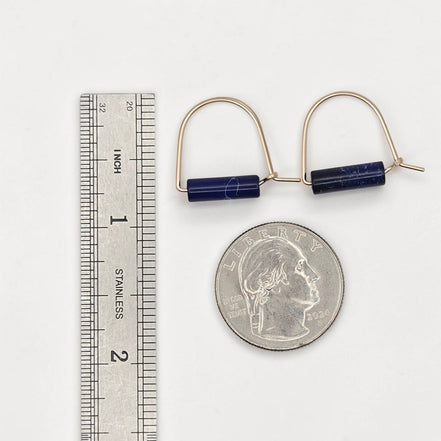 Gold hoop earrings with blue beads next to a ruler and quarter for scale on a white background
