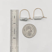 Pair of earrings with marble-like stones next to a ruler and quarter for scale on a white background