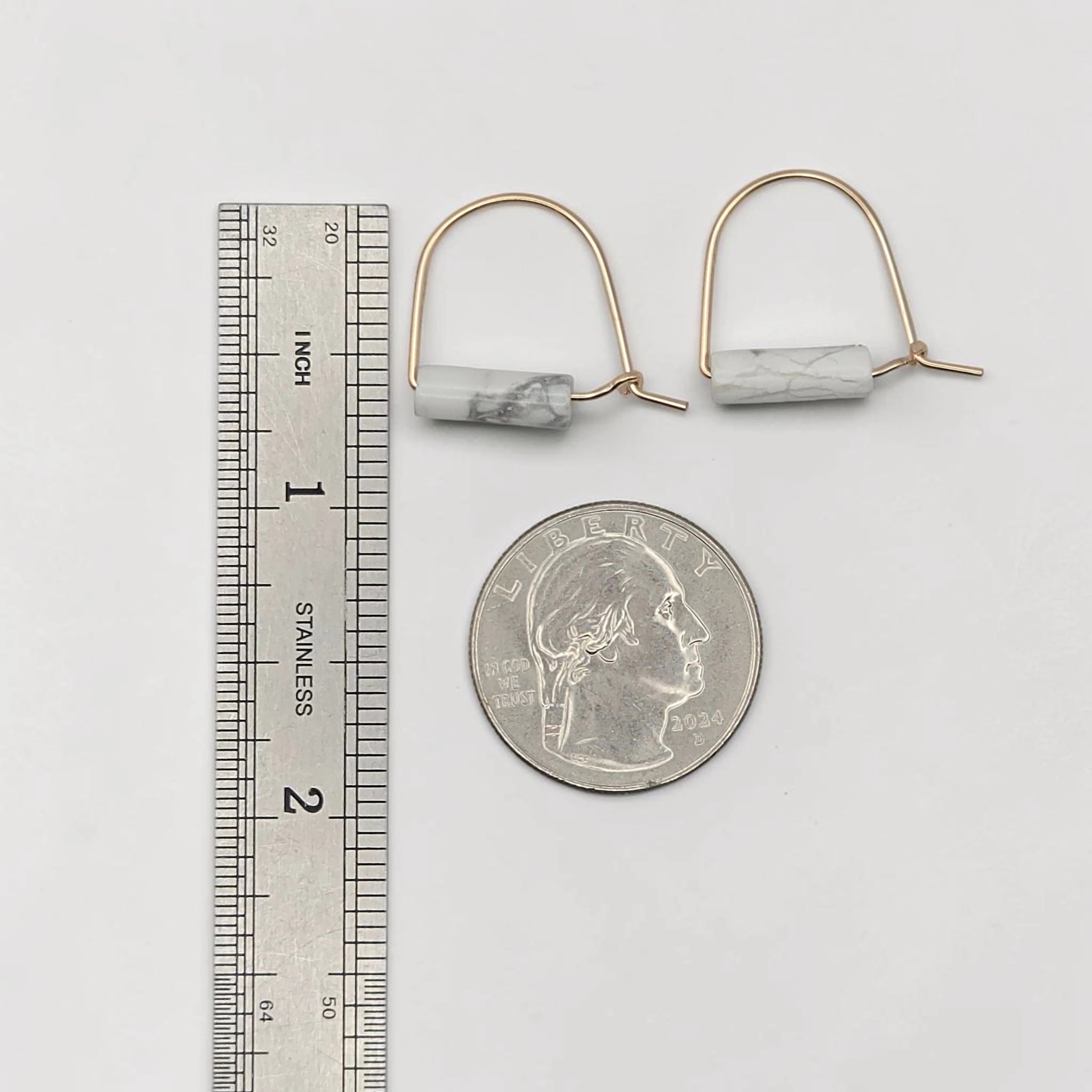 Pair of earrings with marble-like stones next to a ruler and quarter for scale on a white background