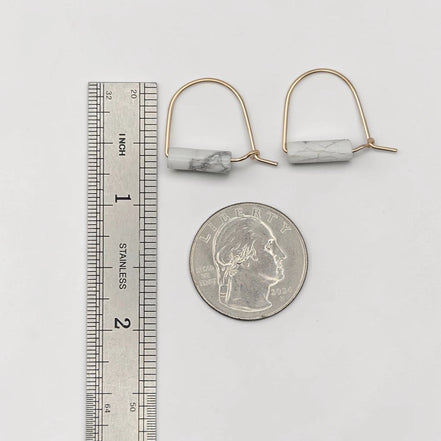Pair of earrings with marble-like stones next to a ruler and quarter for scale on a white background