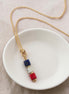 Necklace with red white and blue  beads on a white dish against a beige background