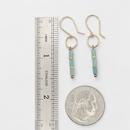 A pair of gold drop earrings with light blue turquoise beads and small gold spacer rings, shown next to a stainless steel ruler and a US quarter for scale on a white background.