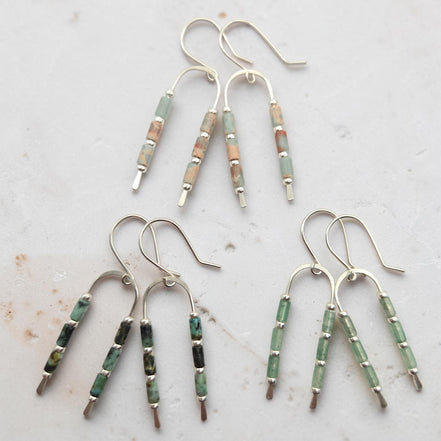 three pairs of silver wishbone shaped earrings. one featuring green aventurine beads, one featuring african turquoise beads and one featuring aqua terra jasper beads