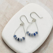 Silver earrings with blue beads on a white stone surface