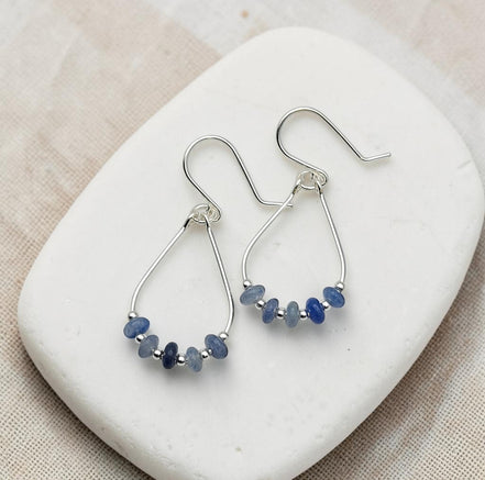 Silver earrings with blue beads on a white stone surface