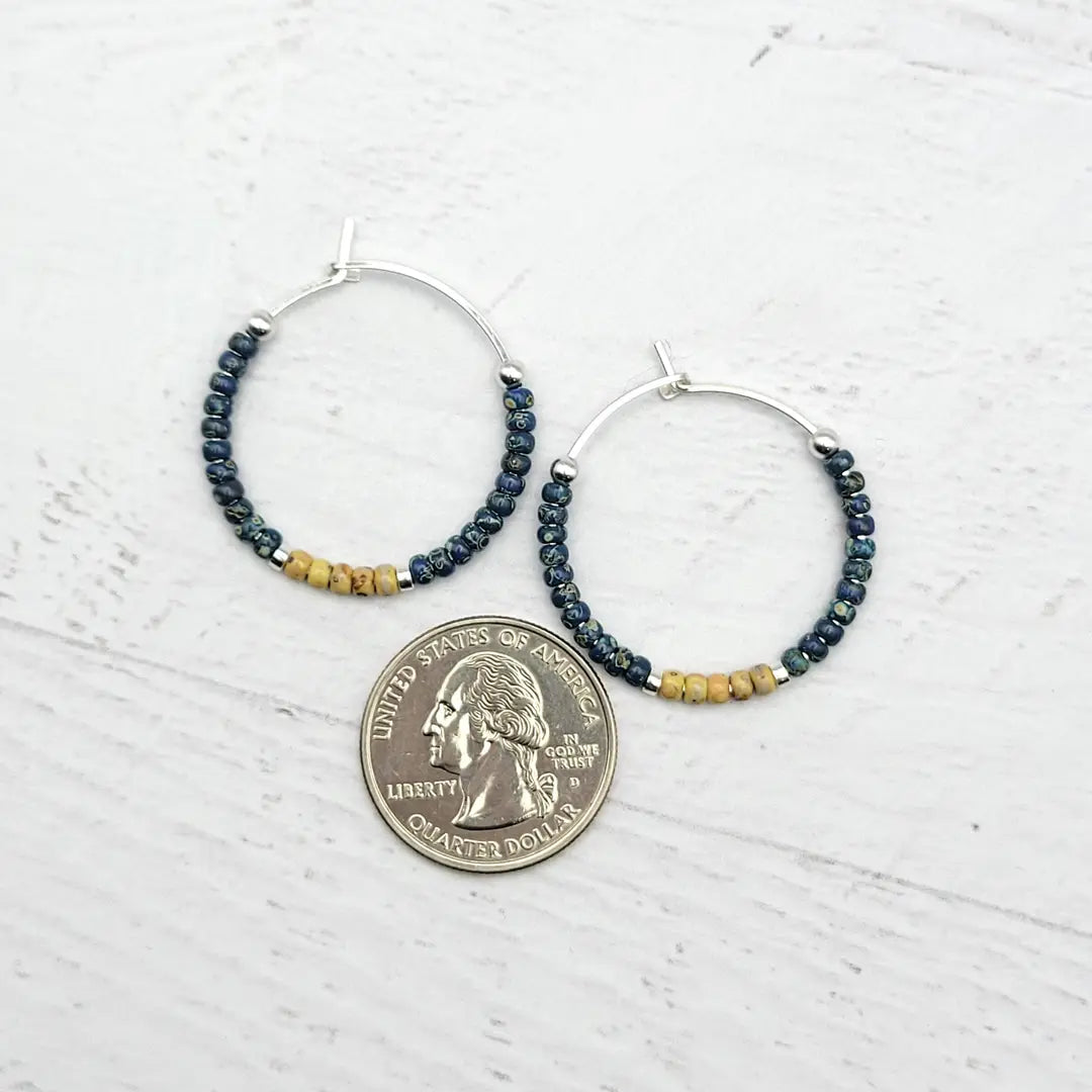 Hoop earrings with beaded accents and a quarter coin charm on a light wooden surface.