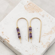 Pair of gold and purple beaded earrings on a marble surface