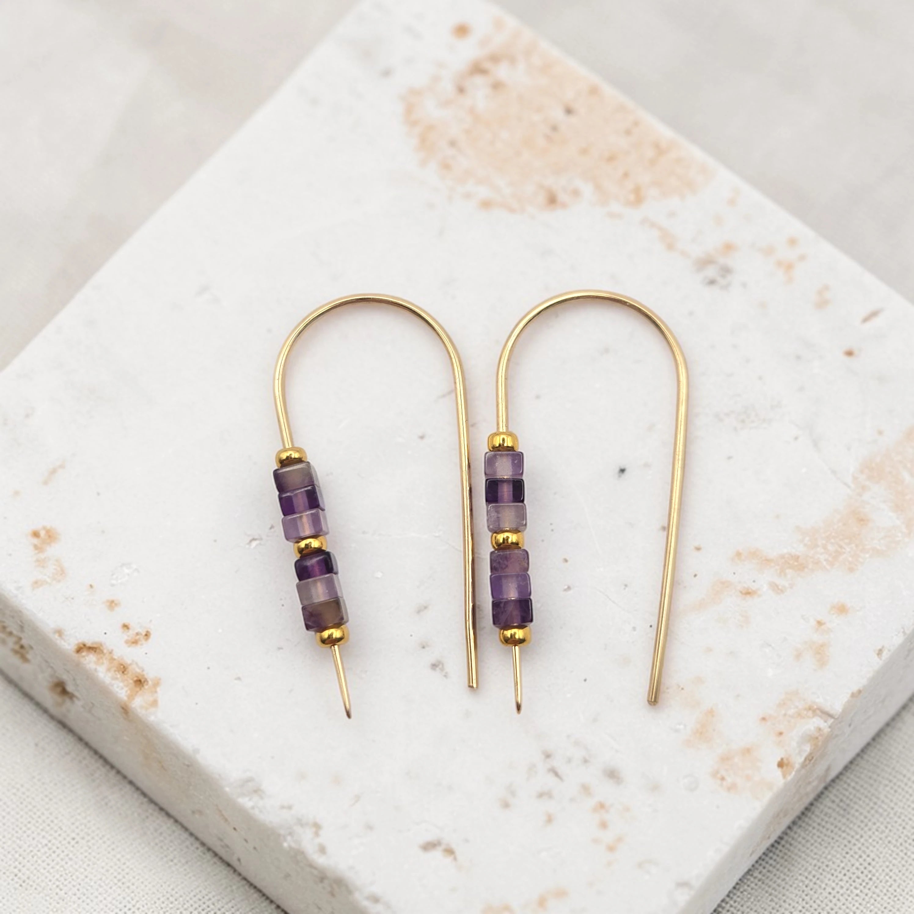 Pair of gold and purple beaded earrings on a marble surface