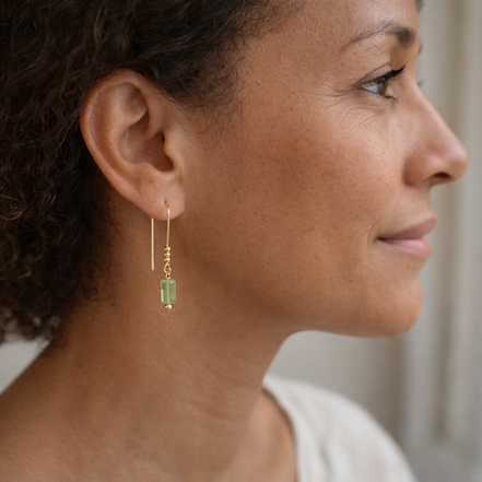 Close-up of a woman wearing gold earrings with green gemstones.