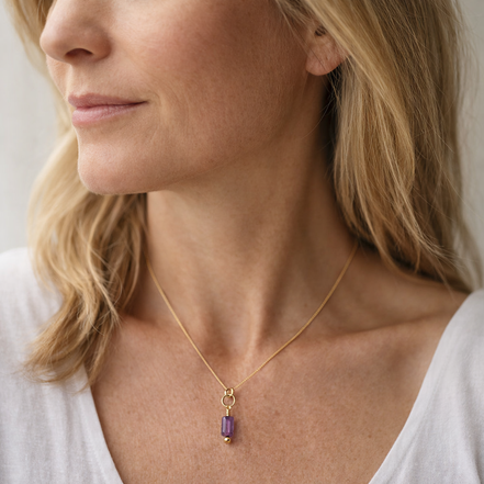 Woman wearing a gold necklace with a purple pendant against a neutral background