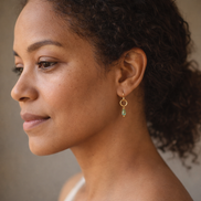 Close-up of a woman wearing a gold earring with a green gemstone against a neutral background
