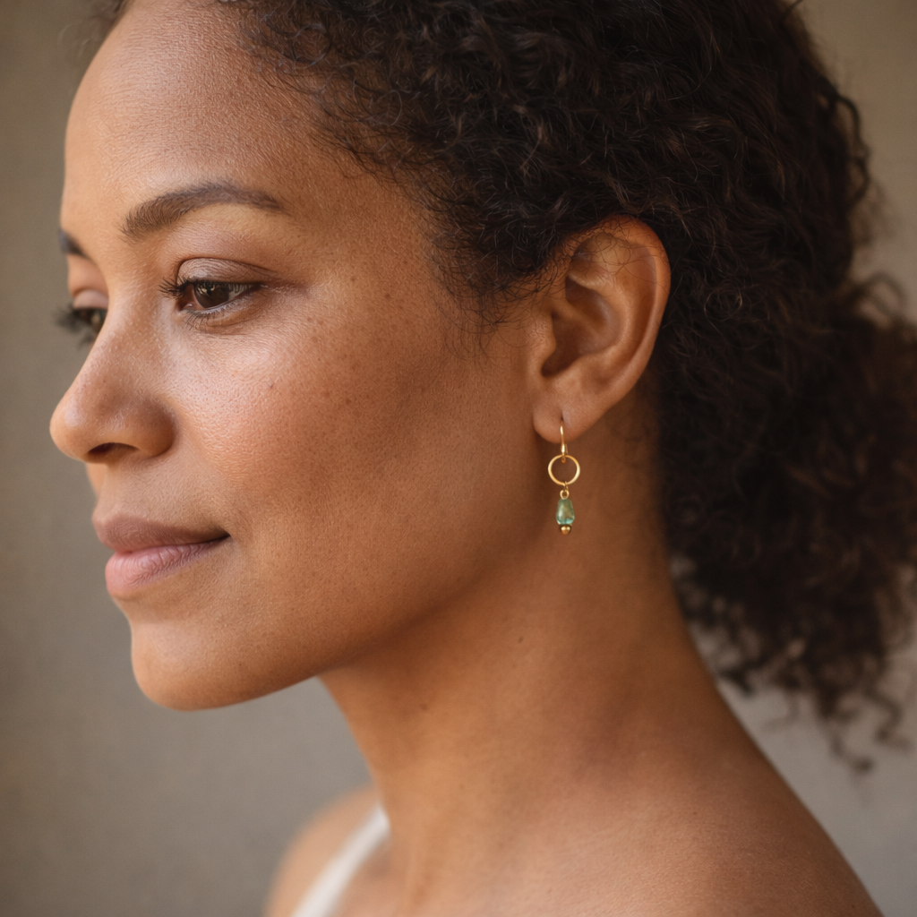 Close-up of a woman wearing a gold earring with a green gemstone against a neutral background