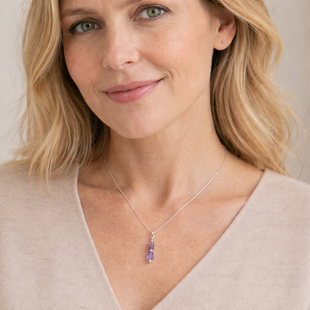 Woman wearing a necklace with a purple pendant against a neutral background