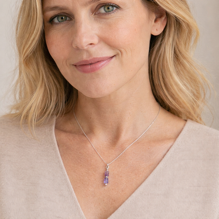 Woman wearing a necklace with a purple pendant against a neutral background