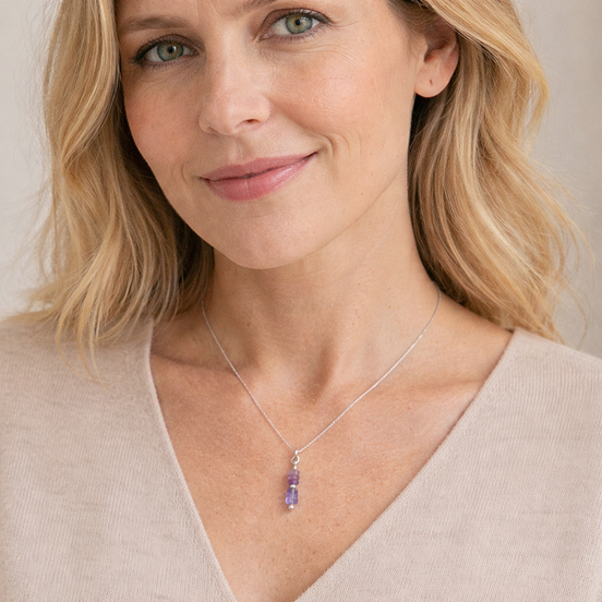 Woman wearing a necklace with a purple pendant against a neutral background