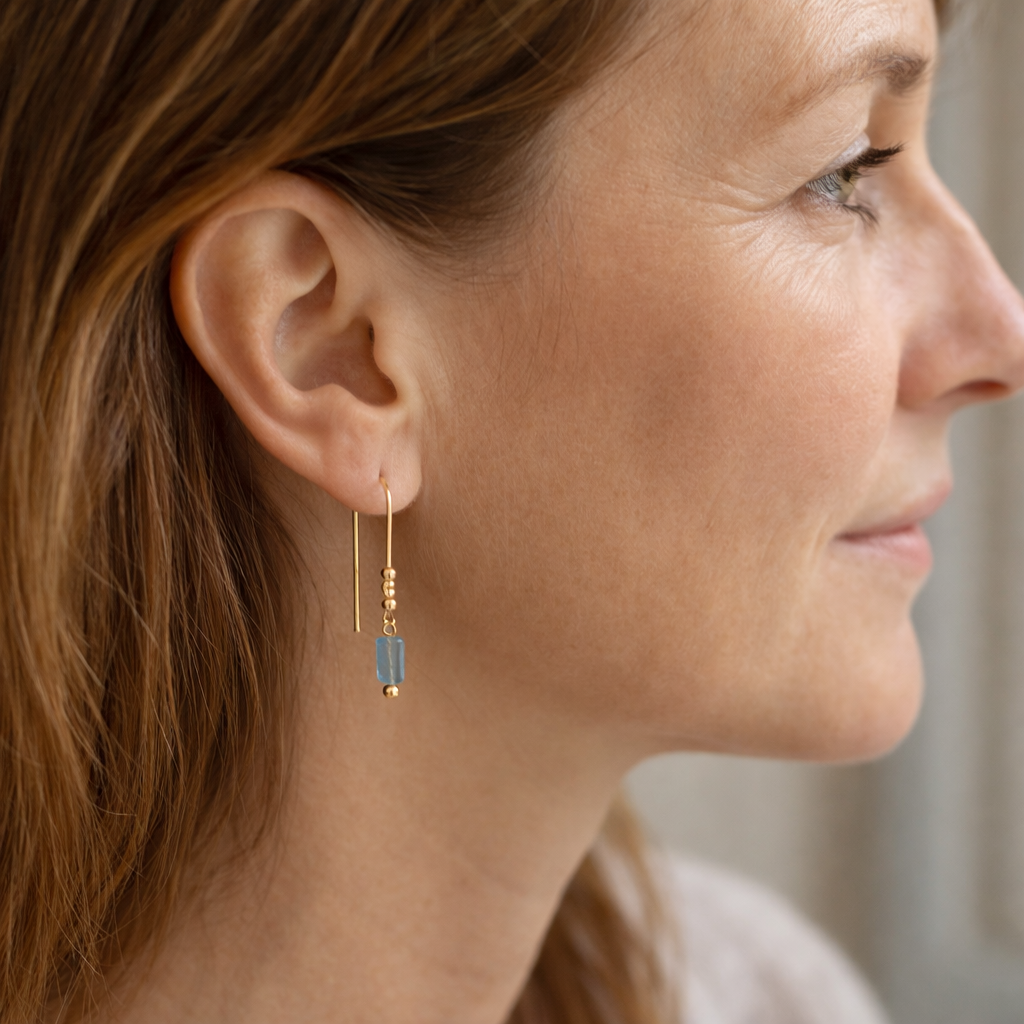 Close-up of a woman wearing gold earrings with a blue gemstone.