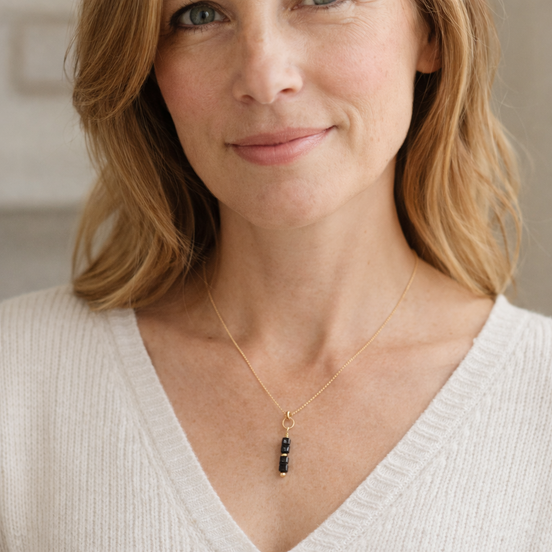 Woman wearing a gold necklace with a pendant, smiling.