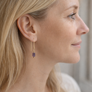 Close-up of a woman wearing a dangling earring with a purple gemstone.
