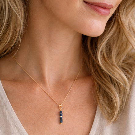 Close-up of a woman wearing a gold necklace with a blue pendant.