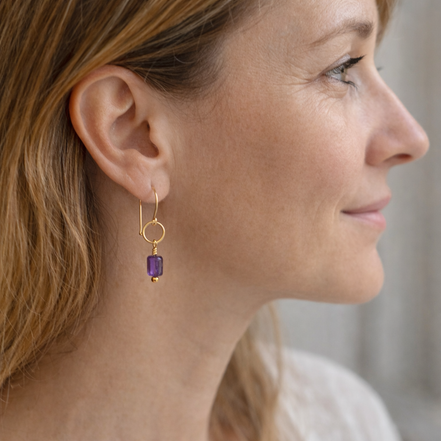 Close-up of a woman wearing gold earrings with purple beads.
