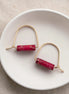 Gold earrings with red cylindrical stones on a white dish