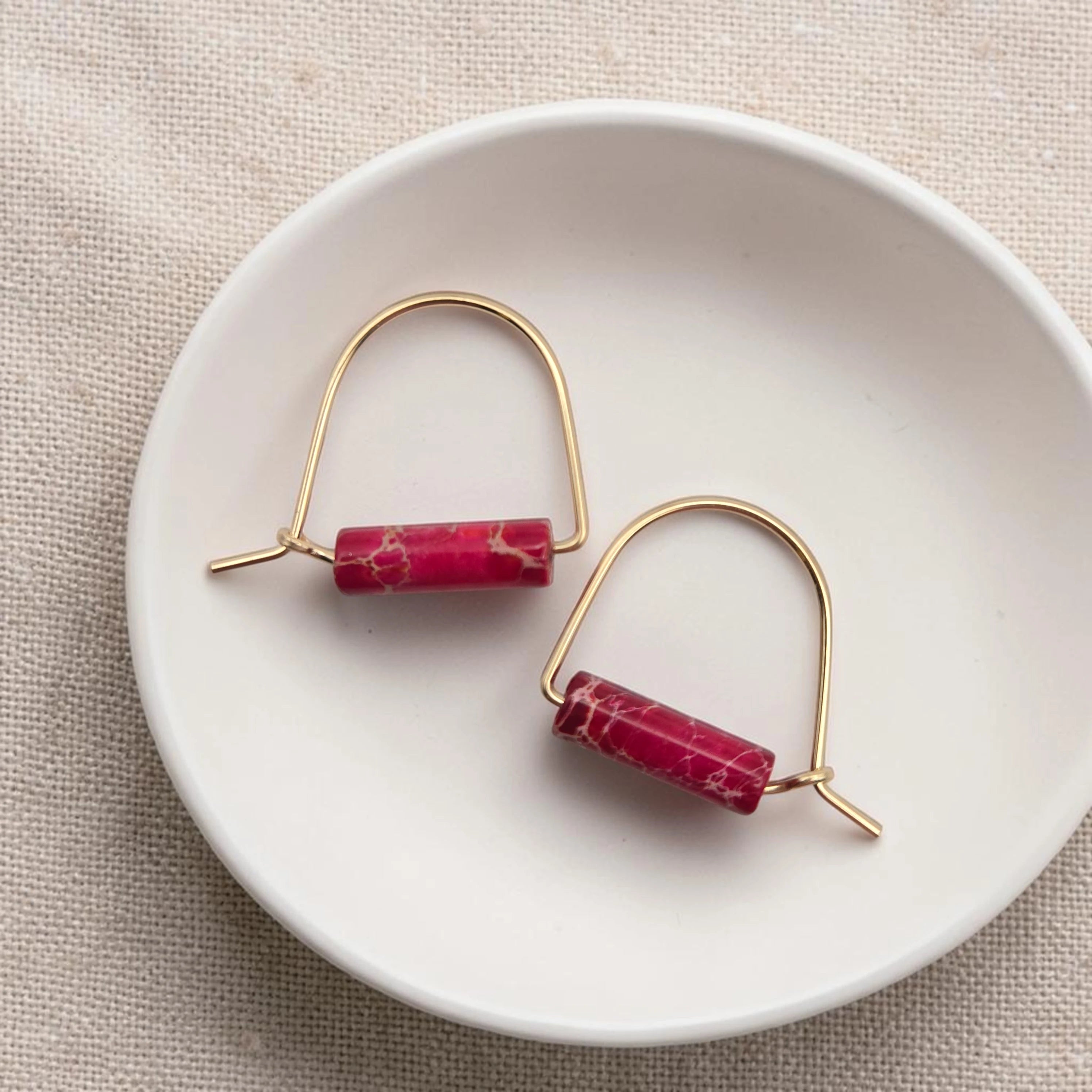 Gold earrings with red cylindrical stones on a white dish