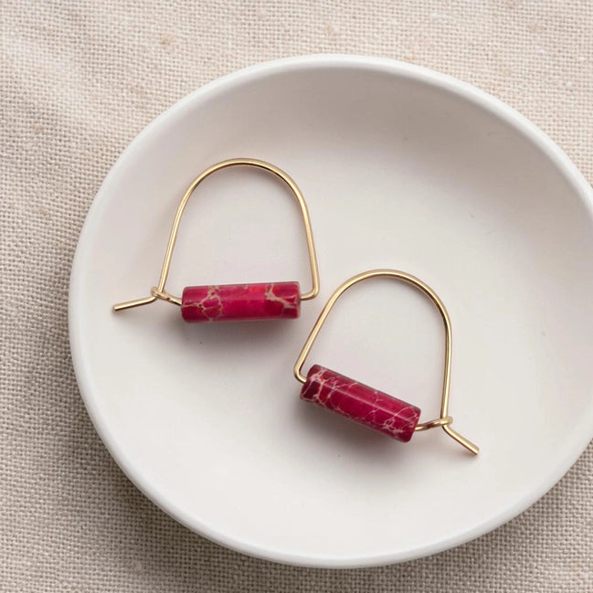 Gold earrings with red cylindrical stones on a white dish