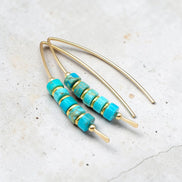 Turquoise beaded earrings with gold accents on a light gray background