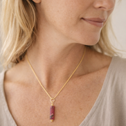 Woman wearing a gold necklace with a red pendant