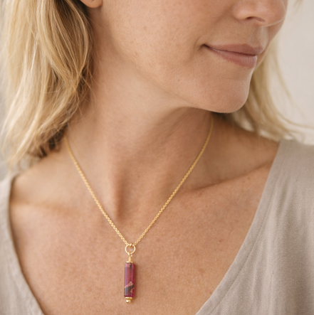 Woman wearing a gold necklace with a red pendant