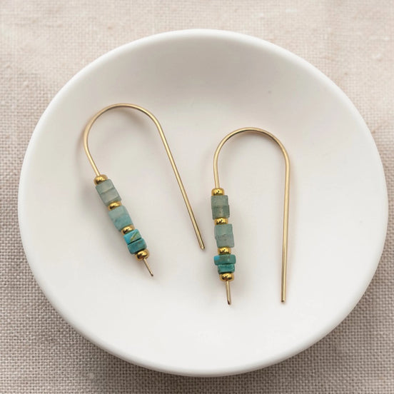 Pair of gold and turquoise beaded earrings on a white dish.