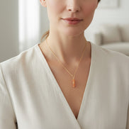 Woman wearing a gold necklace with a pendant in a neutral setting