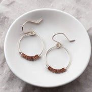 Pair of hoop earrings with brown beads on a white plate.