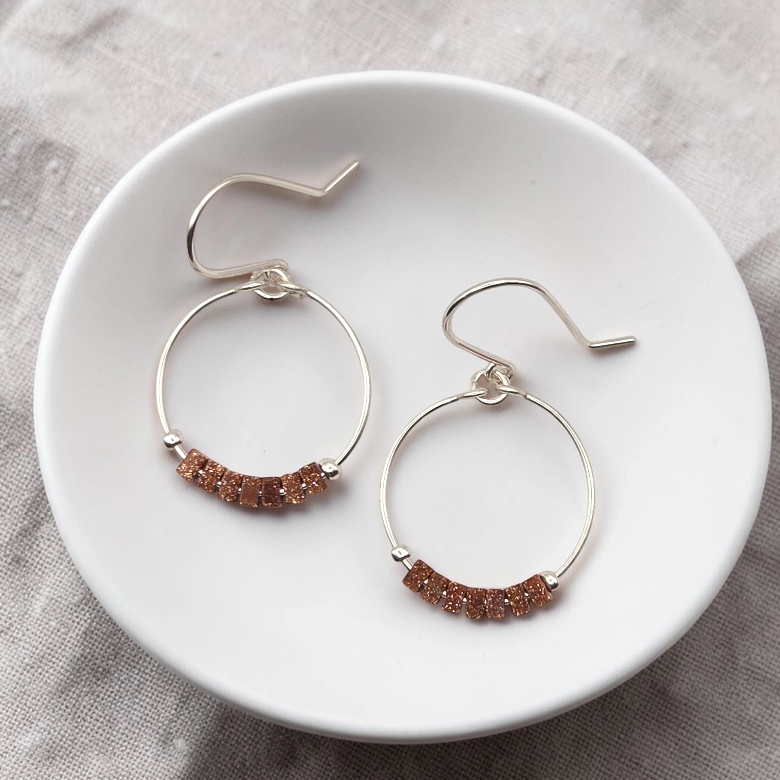 Pair of hoop earrings with brown beads on a white plate.
