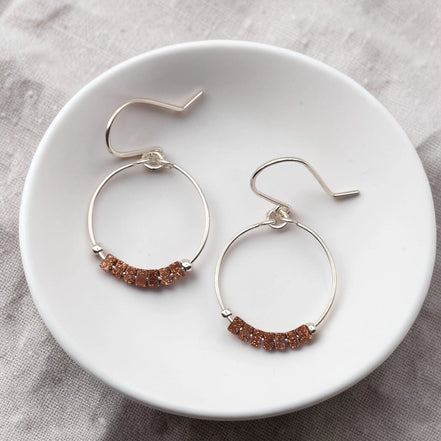 Pair of hoop earrings with brown beads on a white plate.