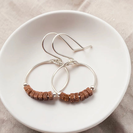 Silver hoop earrings with brown beads on a white plate.
