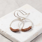 Silver hoop earrings with brown beads on a white stone surface