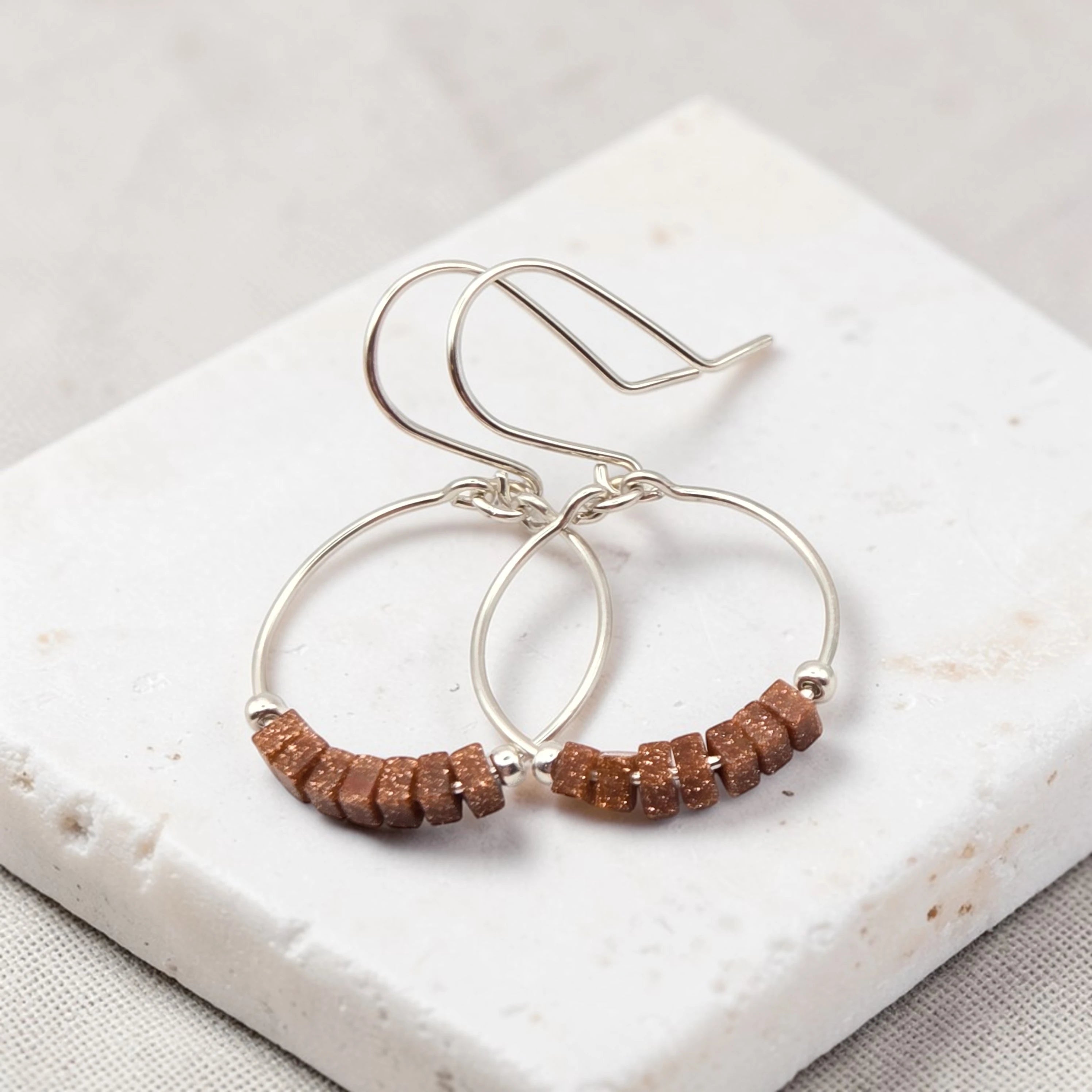 Silver hoop earrings with brown beads on a white stone surface