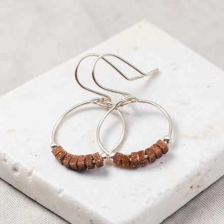Silver hoop earrings with brown beads on a white stone surface