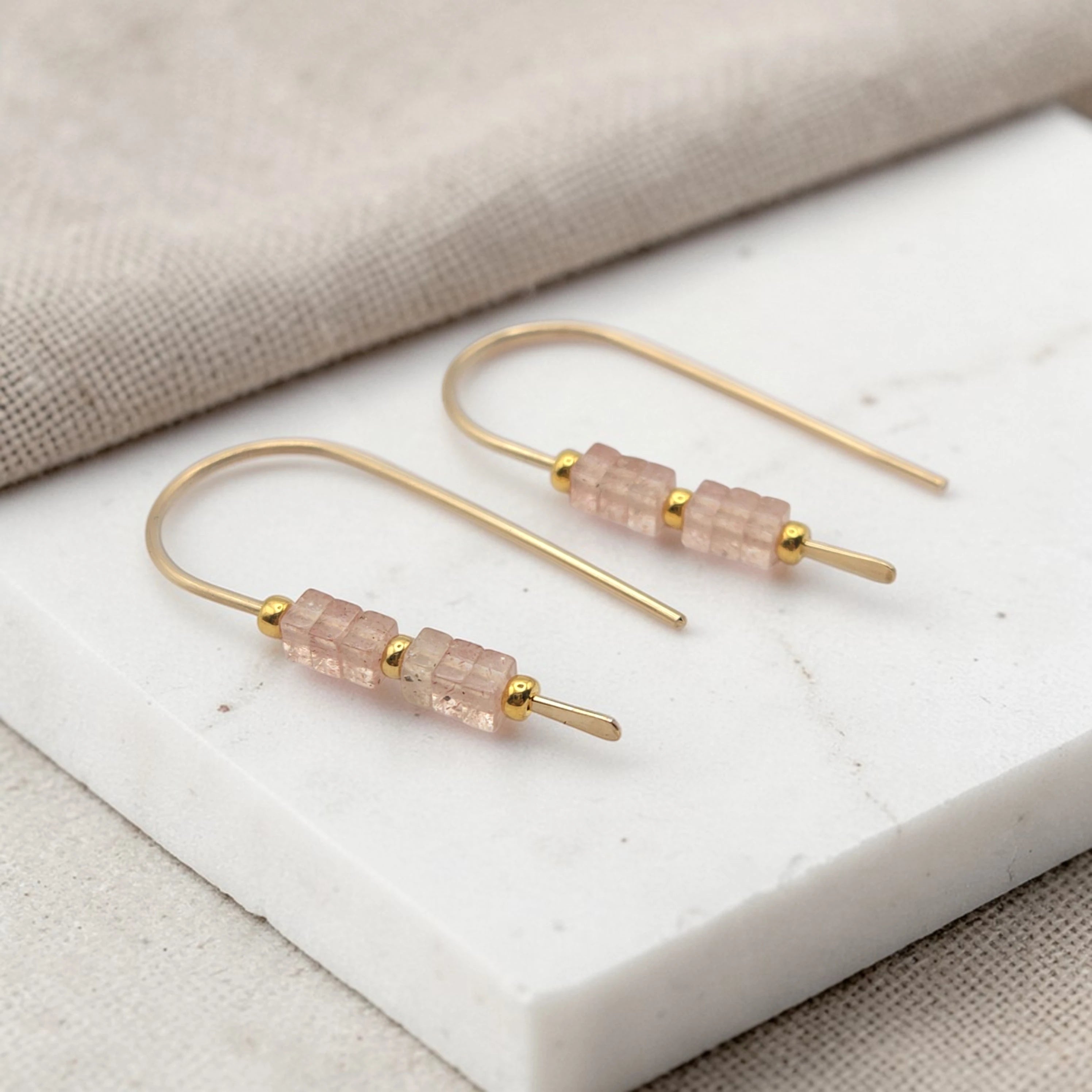 Gold earrings with pink beads on a white stone surface