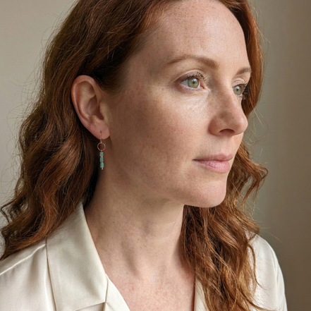Bijou by SAM Riverstone dangle earrings featuring blue-green amazonite gemstones on gold hoops worn by a woman.