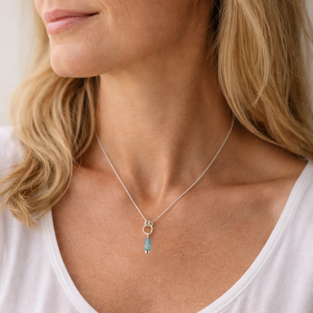 Close-up of a woman wearing a silver necklace with a blue pendant.