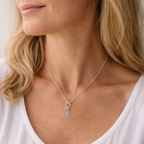 Close-up of a woman wearing a silver necklace with a blue pendant.