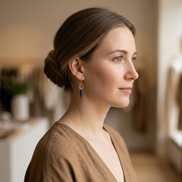 Woman with a bun hairstyle wearing earrings in a softly lit room.