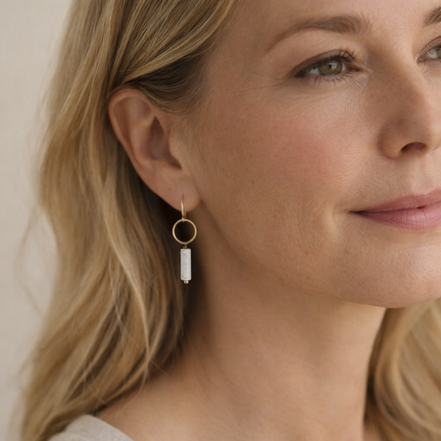 Close-up of a woman wearing gold hoop earrings with a white stone.